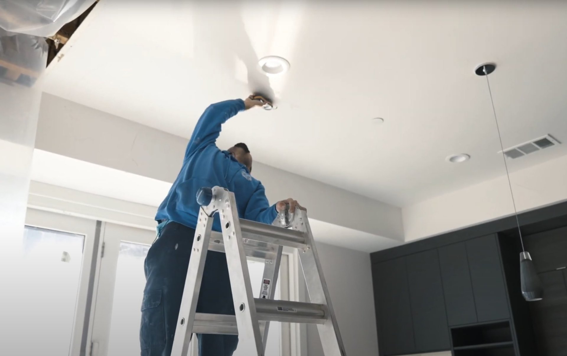 Water damage restoration technician on ladder working on ceiling water damage repair in Johns Creek home with professional equipment visible